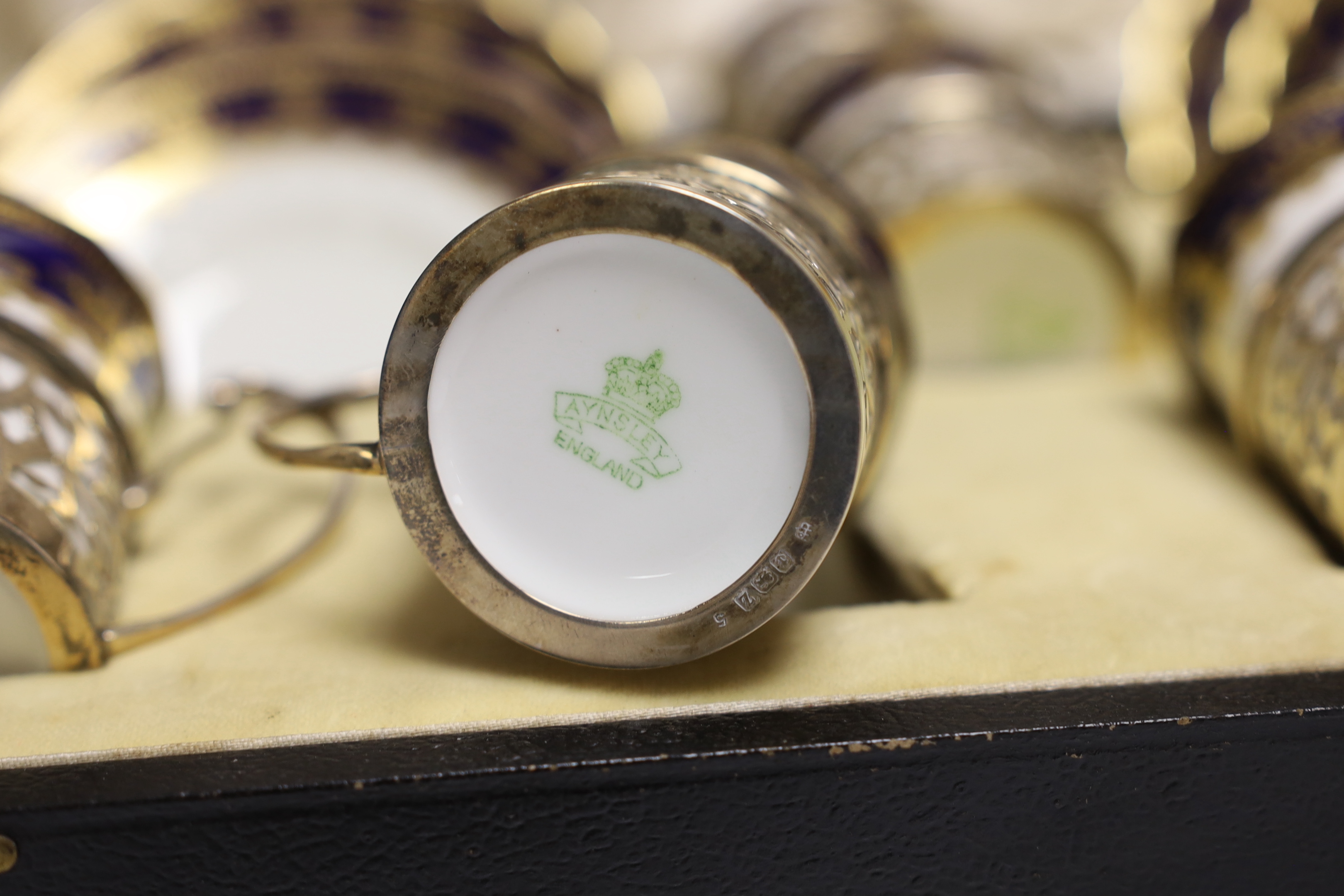 A cased George V set of six Aynsley coffee cans and saucers, the cans with pierced silver holders, C.S. Green & Co, Birmingham, 1924, can 57mm.